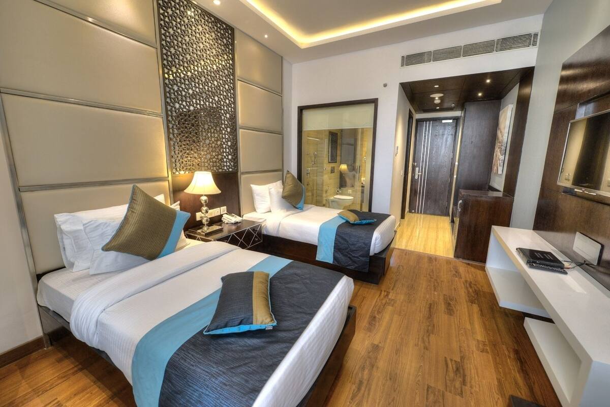 A hotel room with two beds, a desk, a mirror, and a shower area.