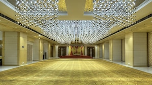 A spacious hall with a patterned carpet and a stage with red curtains. - Hotel Delite Grand (Faridabad)