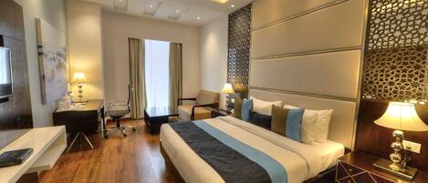 A modern hotel room with a large bed, a desk, a chair, and a TV.