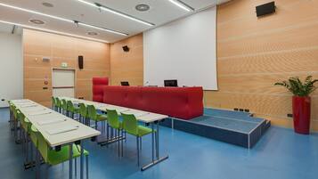 Une salle de conférence avec une longue table, des chaises vertes, un canapé rouge et un écran de projection.