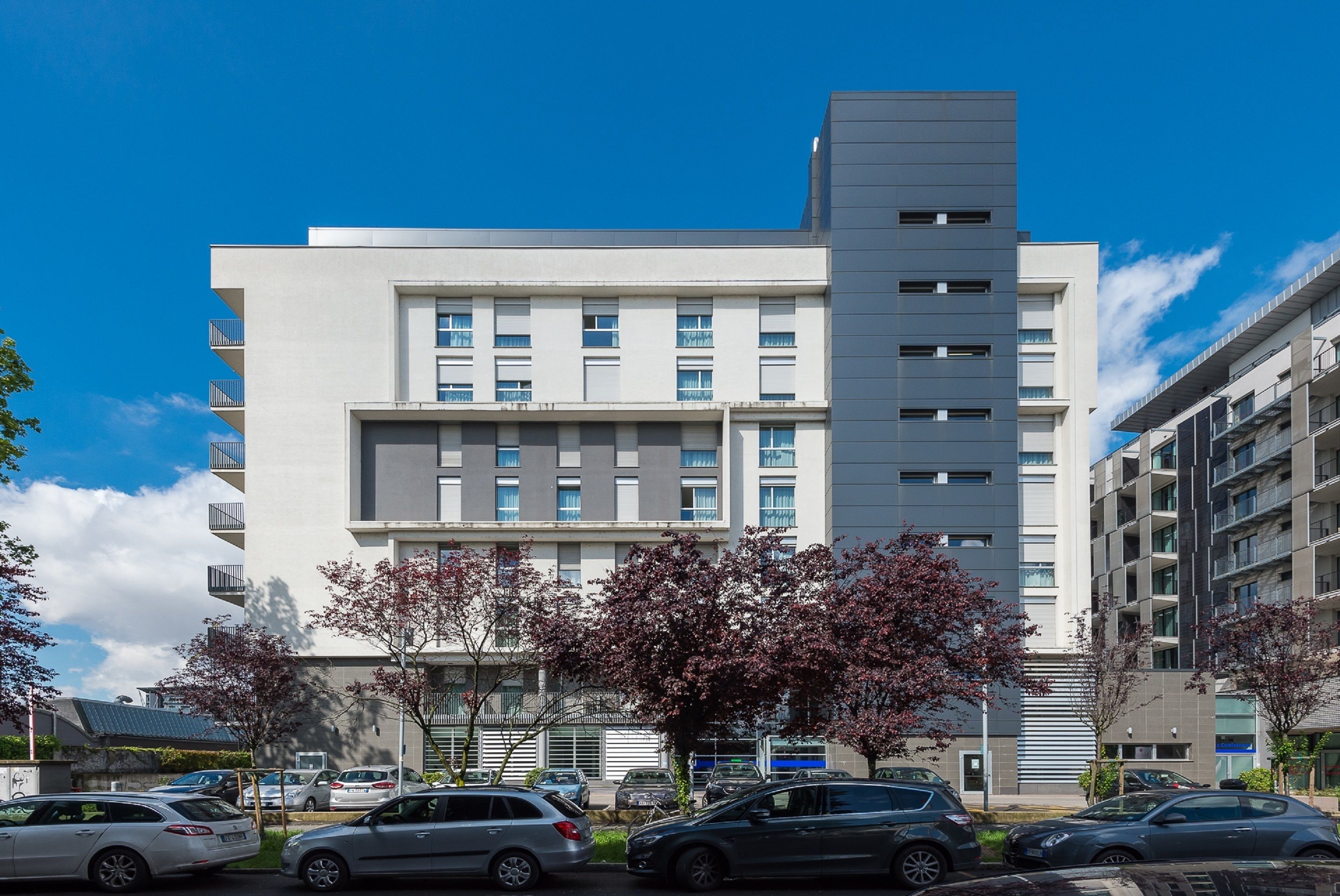 A modern multi-story building with a flat roof, large windows, and balconies.