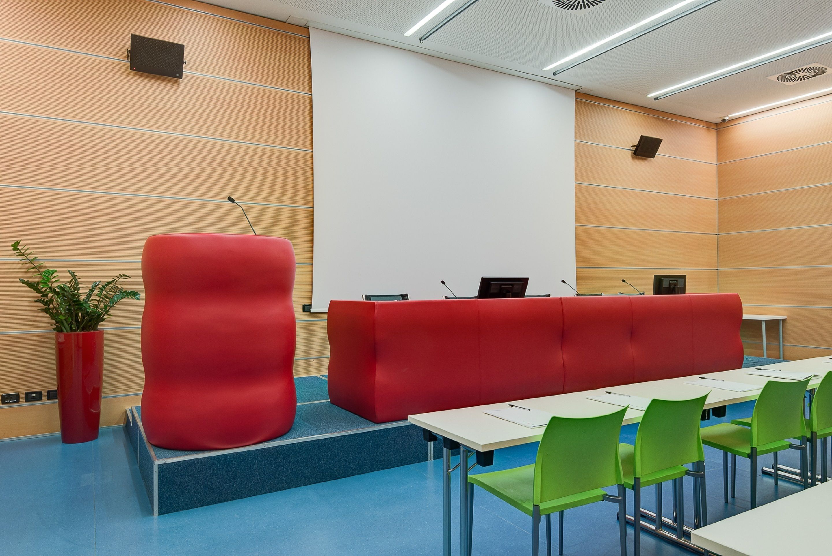 A modern conference room with a red podium, green chairs, and a white table.