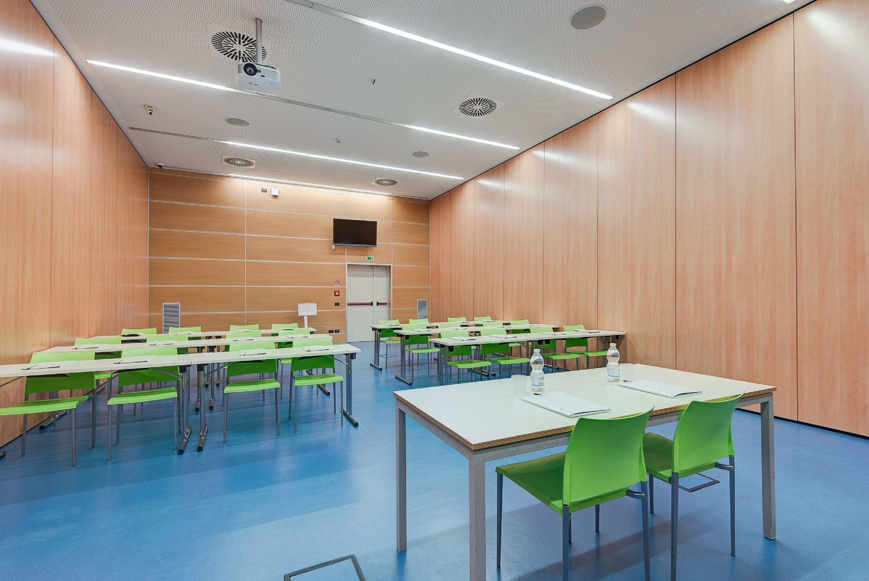 A conference room with multiple tables and chairs, a projector, and a screen on the wall.