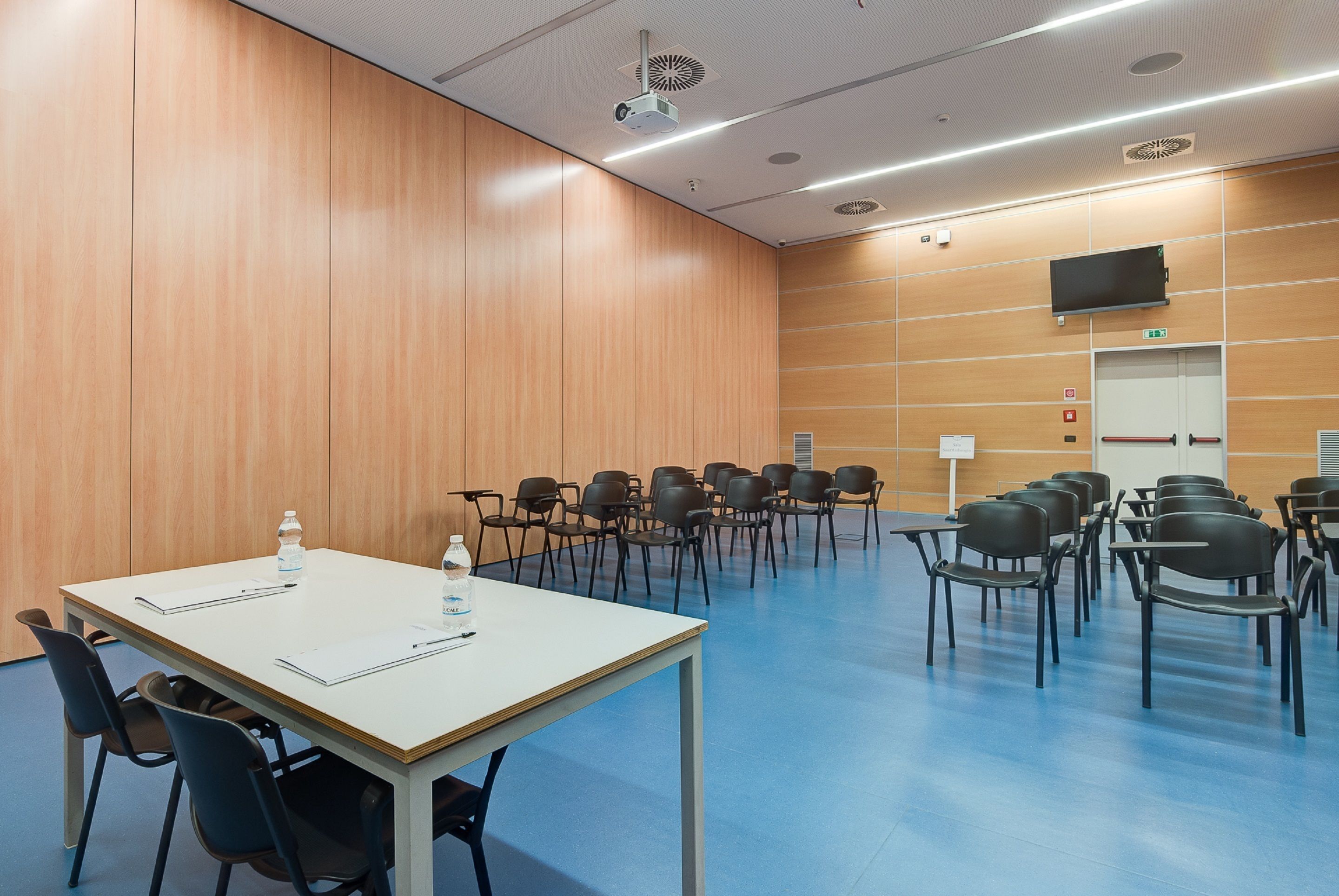 A conference room with a white table, black chairs, and a projector.