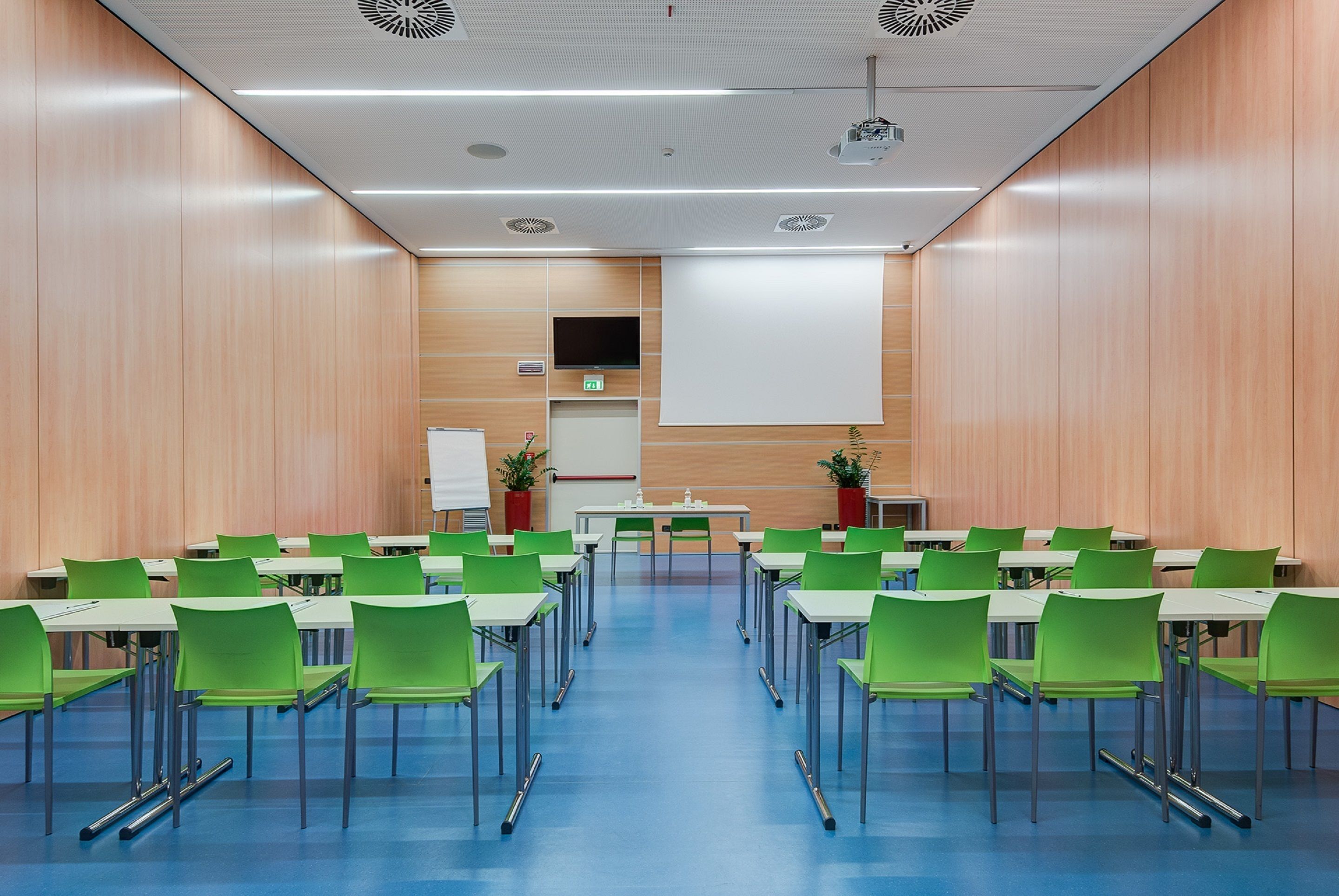 A conference room with green chairs and tables, a whiteboard, and a projector screen.