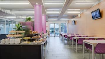 Eine Cafeteria mit einer langen Theke, gefüllt mit verschiedenen Speisen, einem Sitzbereich mit violetten Stühlen und einem großen Fenster mit Blick ins Freie.
