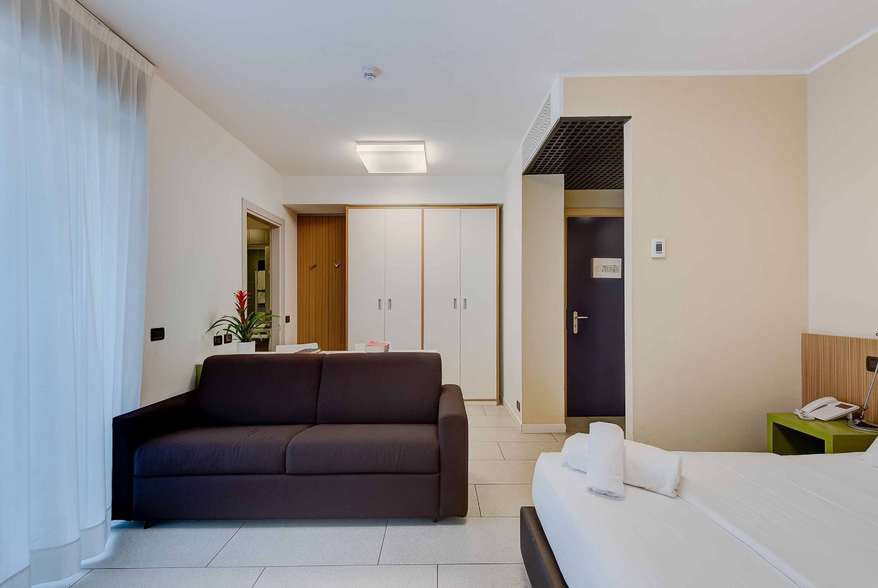 A modern hotel room with a sofa, a bed, a desk, and a wardrobe.