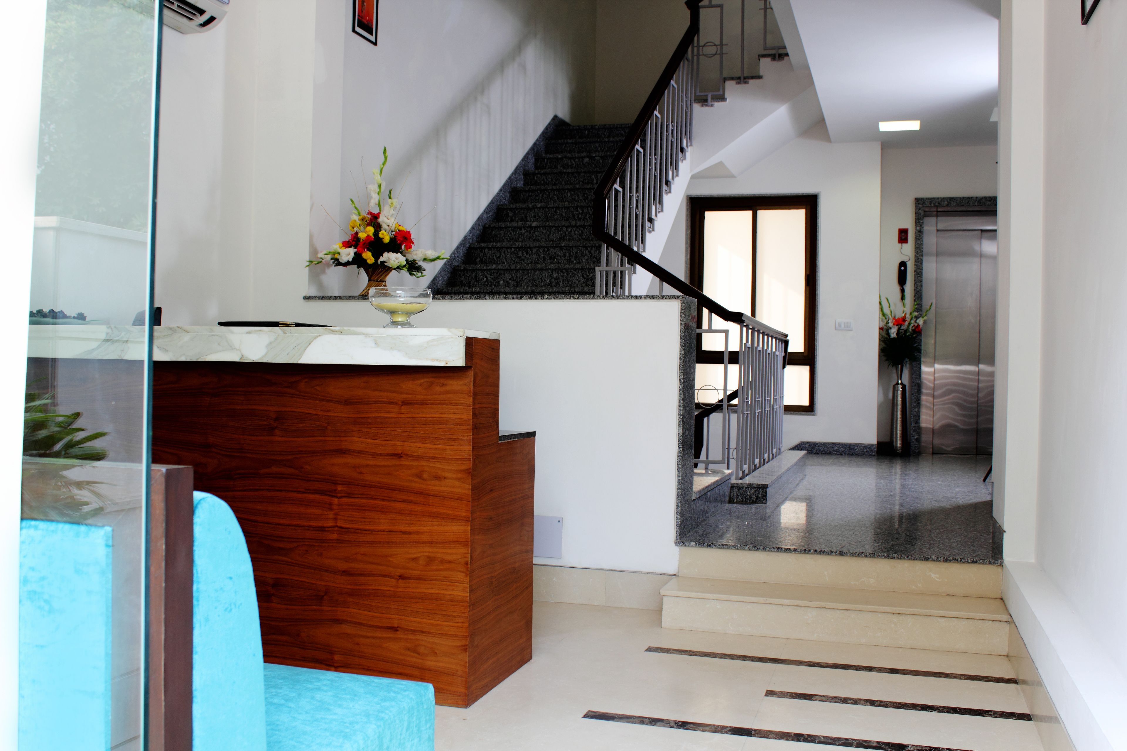 A reception area with a wooden desk, a glass partition, and a staircase leading to an elevator.
