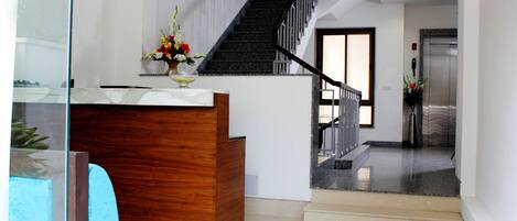 A reception area with a wooden desk, a glass partition, and a staircase leading to an elevator.