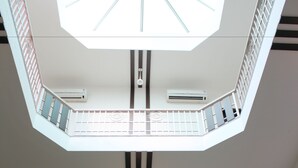 A multi-level interior with a central open space, railings, and hanging lights. - Stately Suites MG Road (Gurugram)