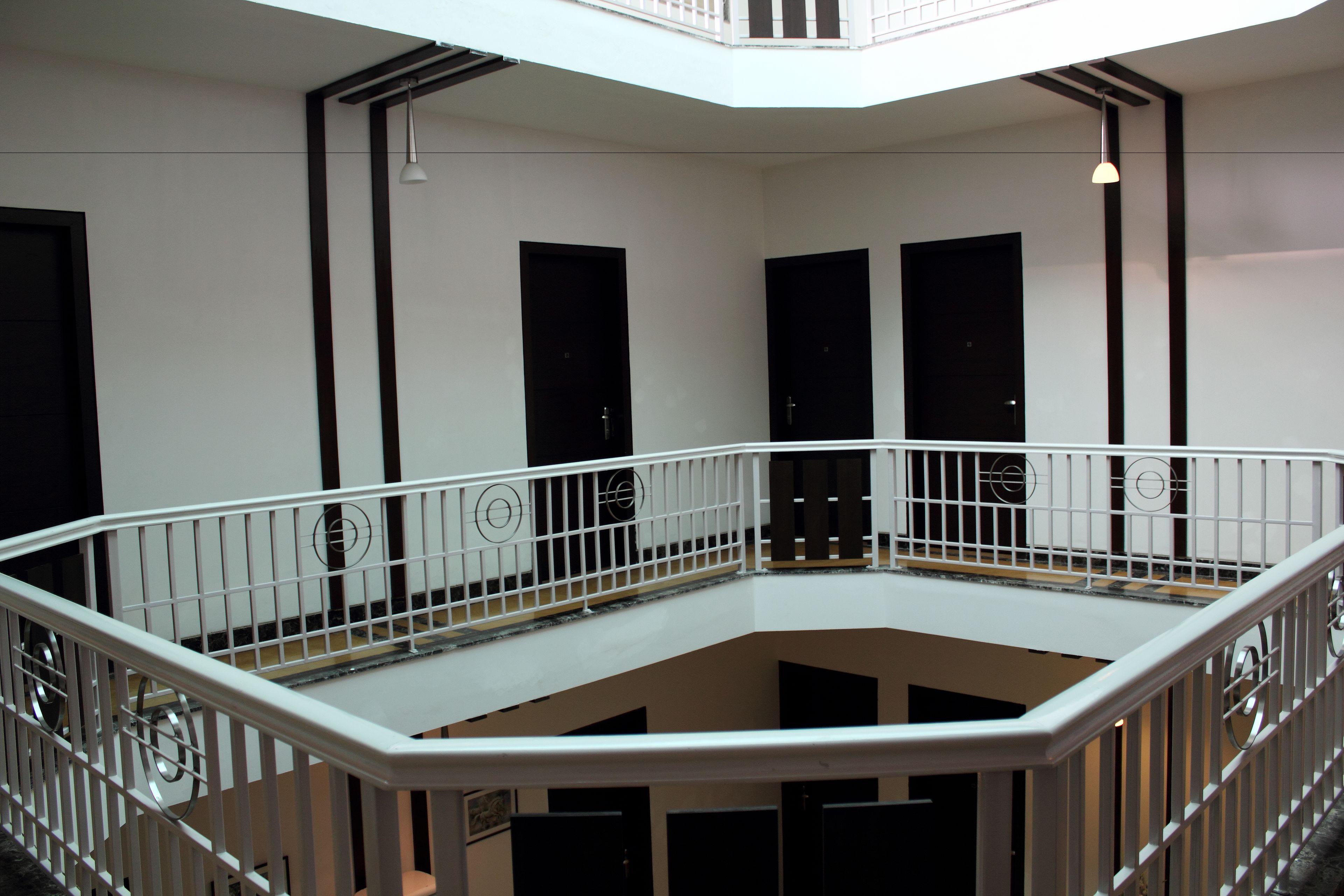 A multi-level interior with a white railing, black doors, and a ceiling light.