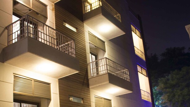 A multi-story building with balconies, air conditioning units, and a well-lit entrance area. - Stately Suites MG Road (Gurugram)