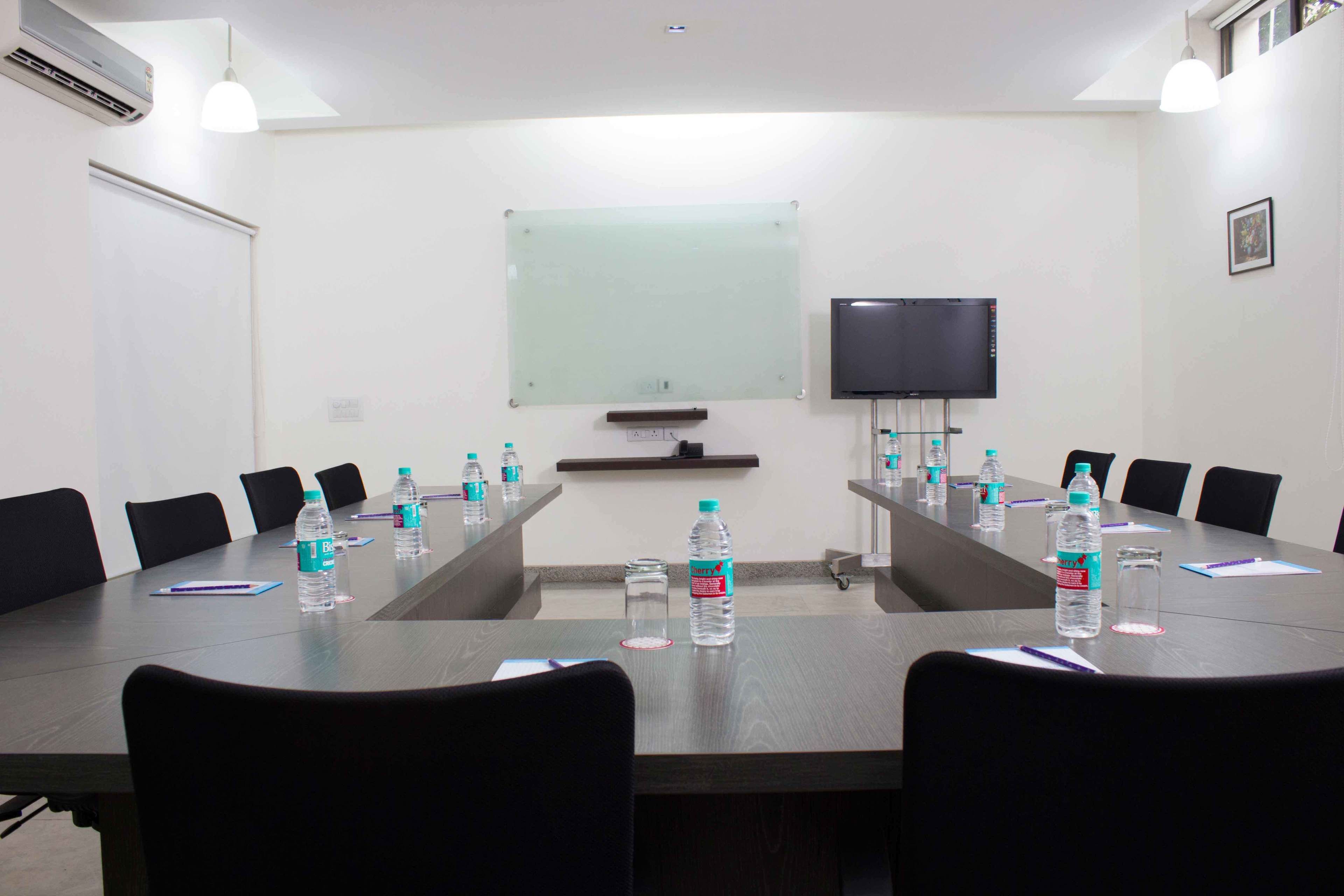 A conference room with a long table, chairs, a projector screen, and a television.