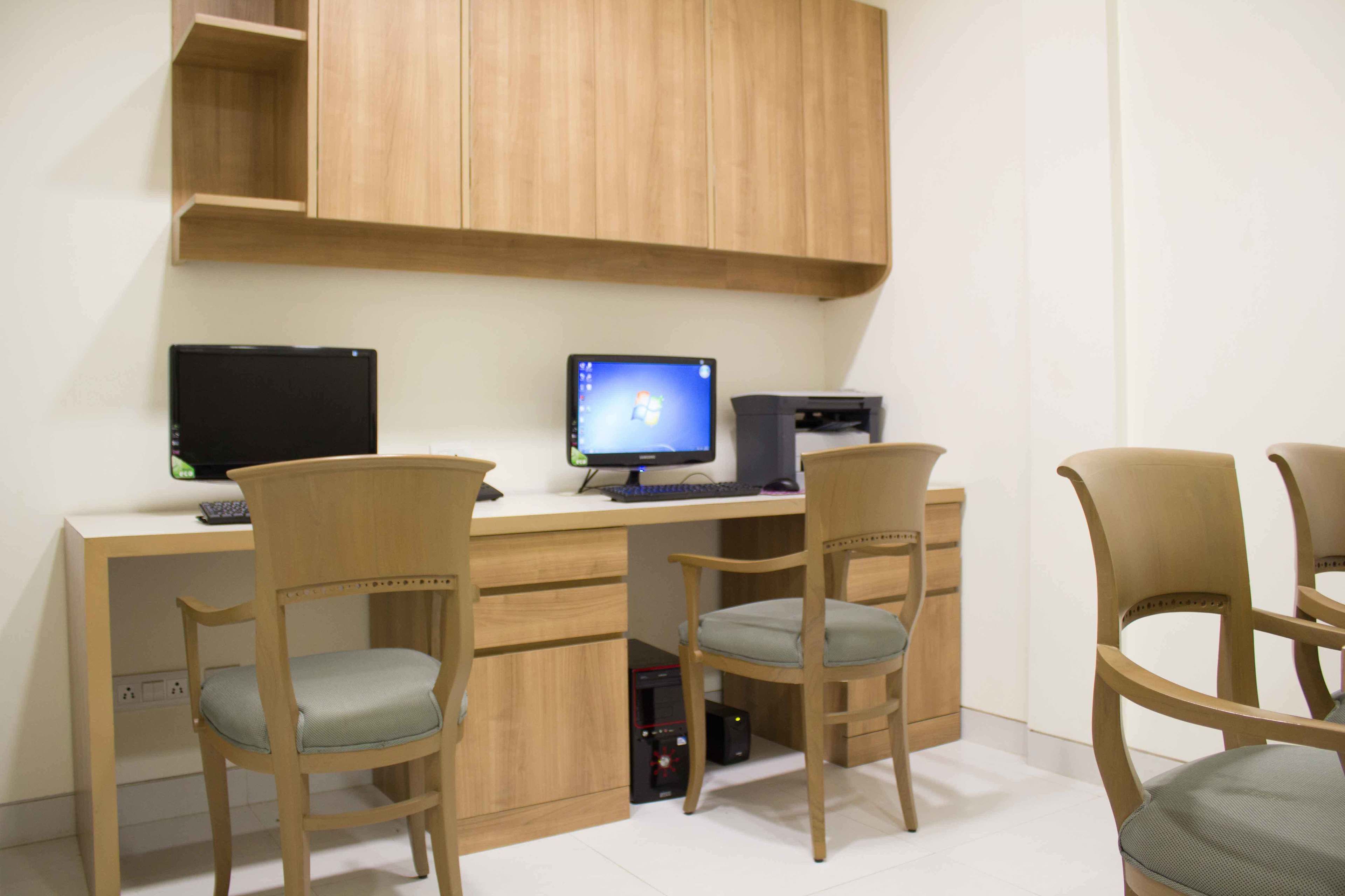 A room with a wooden desk, two chairs, a computer monitor, and a printer.