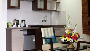 A modern kitchen with dark wooden cabinets, a built-in stove, and a compact refrigerator. - Stately Suites MG Road (Gurugram)