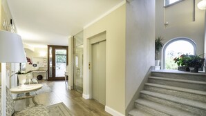 A spacious hallway with a staircase, a dining area with a table and chairs, and a view of the outdoors through a large window. - Locanda Borgo Vecchio (Neive)