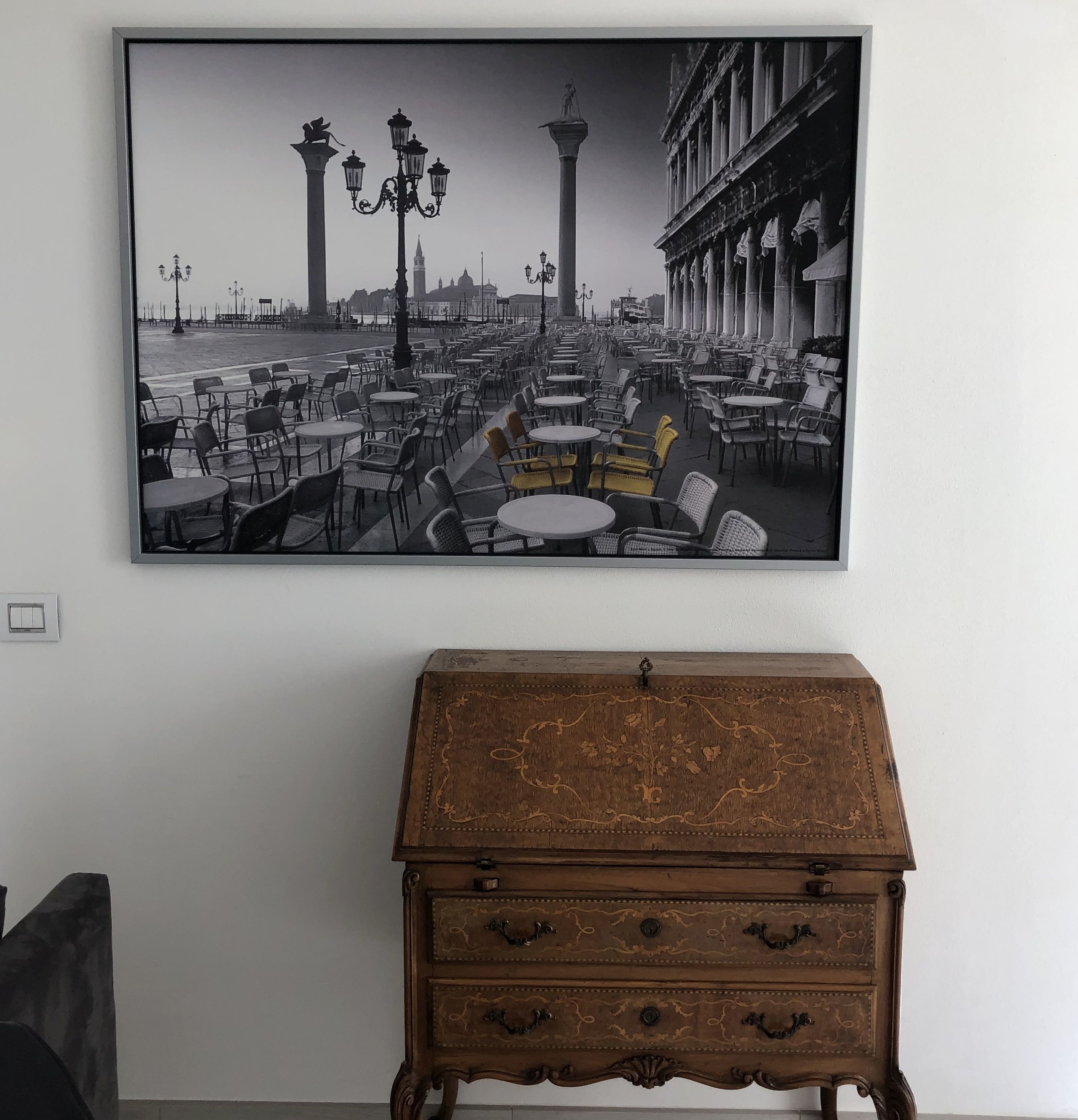Une photographie en noir et blanc, encadrée, représente une vue urbaine avec des cafés et un bâtiment historique. En dessous, on peut voir un coffre en bois orné de sculptures complexes.