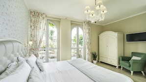 A bedroom with a large bed, a green armchair, a white wardrobe, and a TV on the wall. - Locanda Borgo Vecchio (Neive)