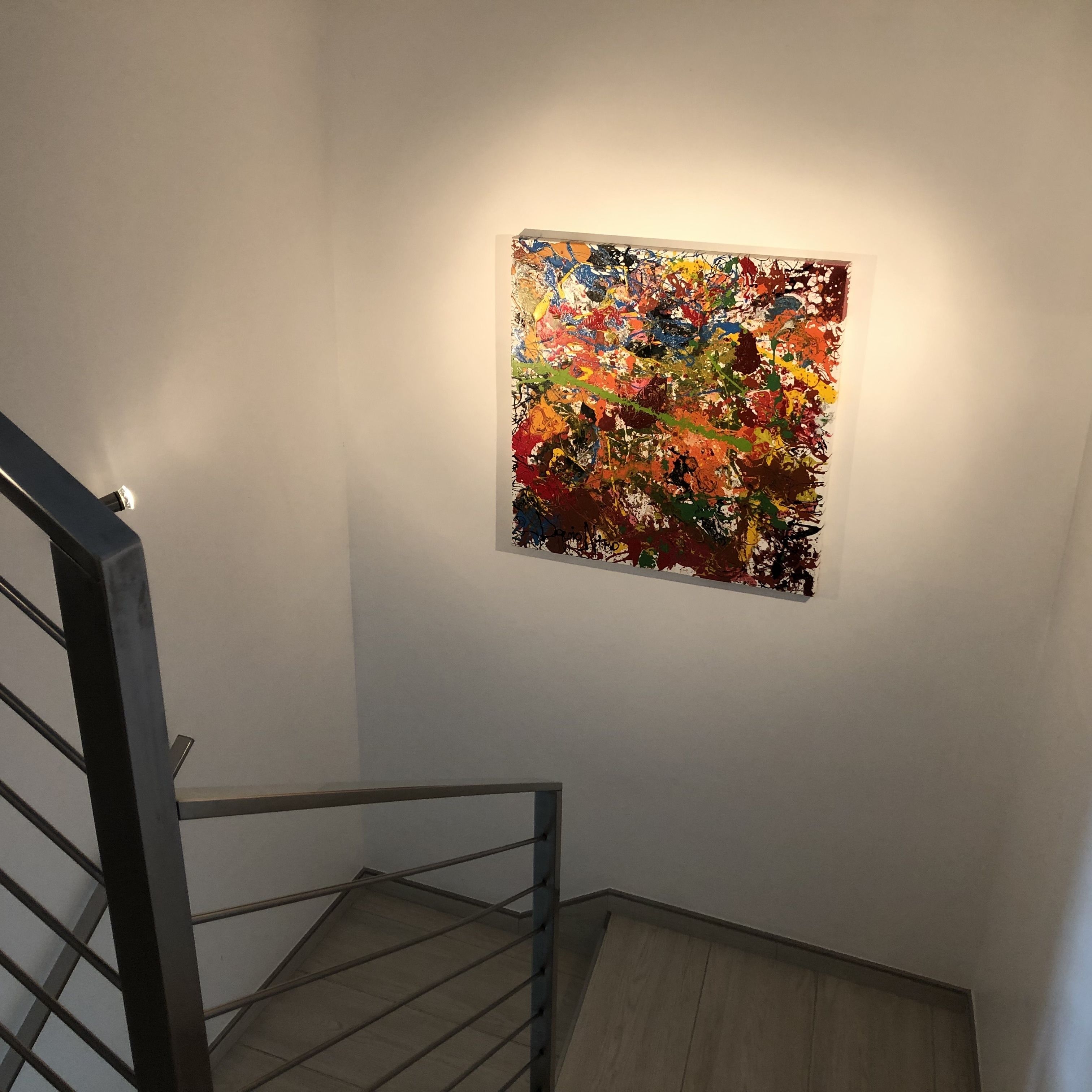 Una escalera con barandilla de metal y un cuadro abstracto de colores en la pared superior.