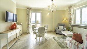 A living room with a TV, dining table, chairs, sofa, and a window with curtains. - Locanda Borgo Vecchio (Neive)