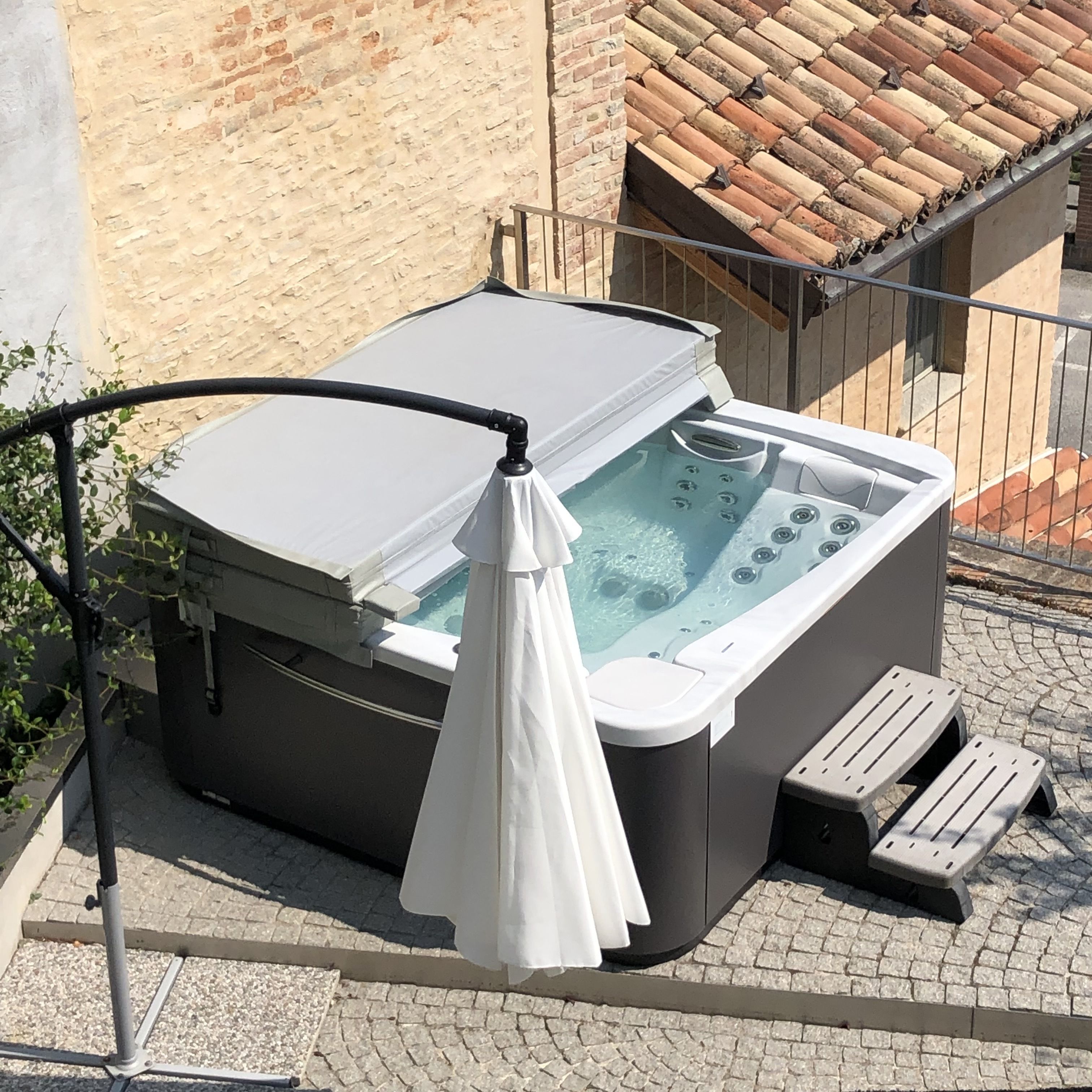 Un bain à remous doté d’une couverture blanche, d’un banc en bois et d’une rambarde en métal.