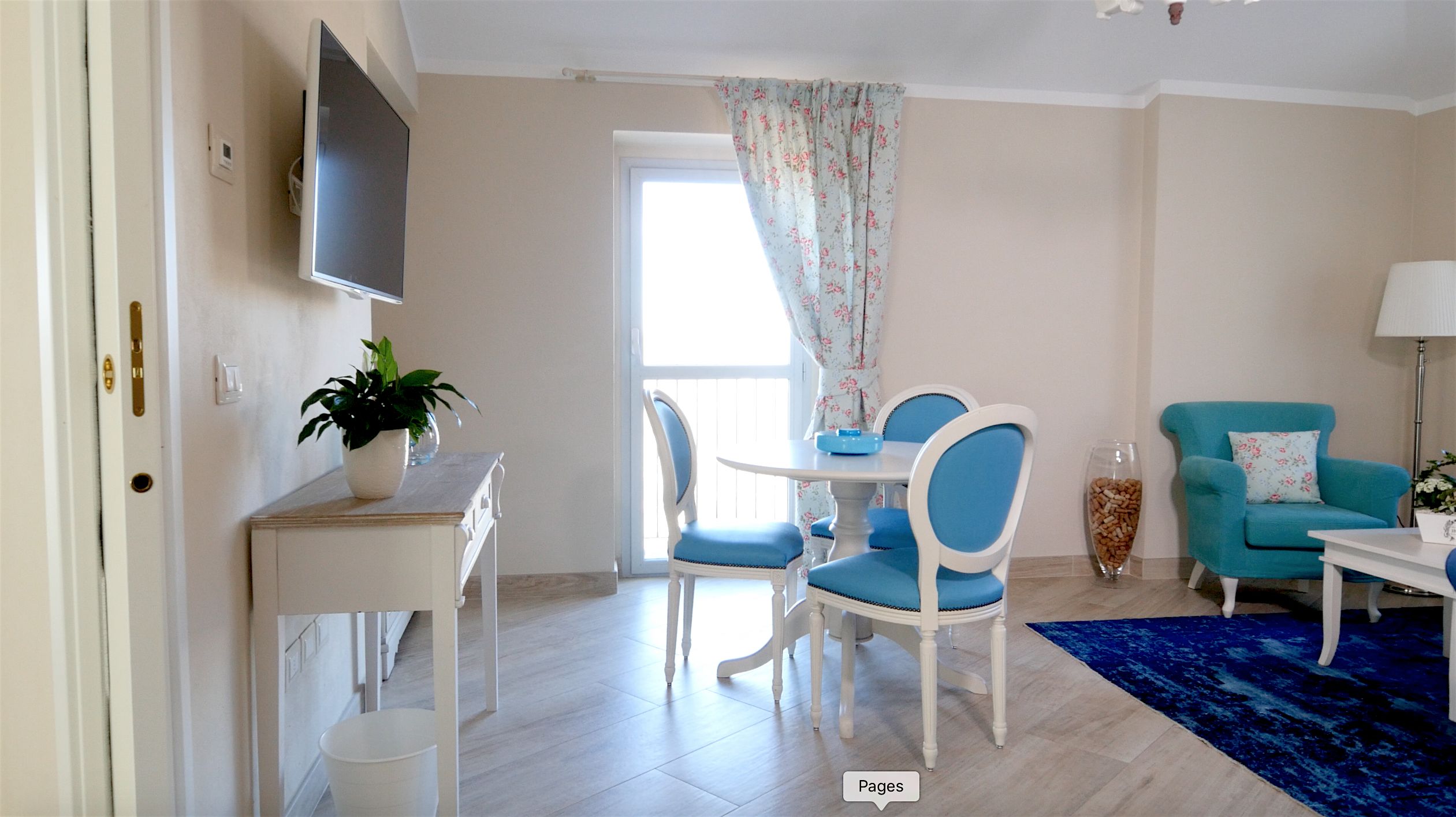 A living room with a TV, a dining table with chairs, a potted plant, and a blue armchair.