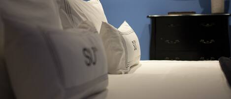 A bed with white bedding and pillows, a dark wooden dresser, and a blue wall with a decorative golden object.