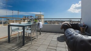Une terrasse sur le toit, avec une table et des chaises, un barbecue et une vue sur la ville et la mer.