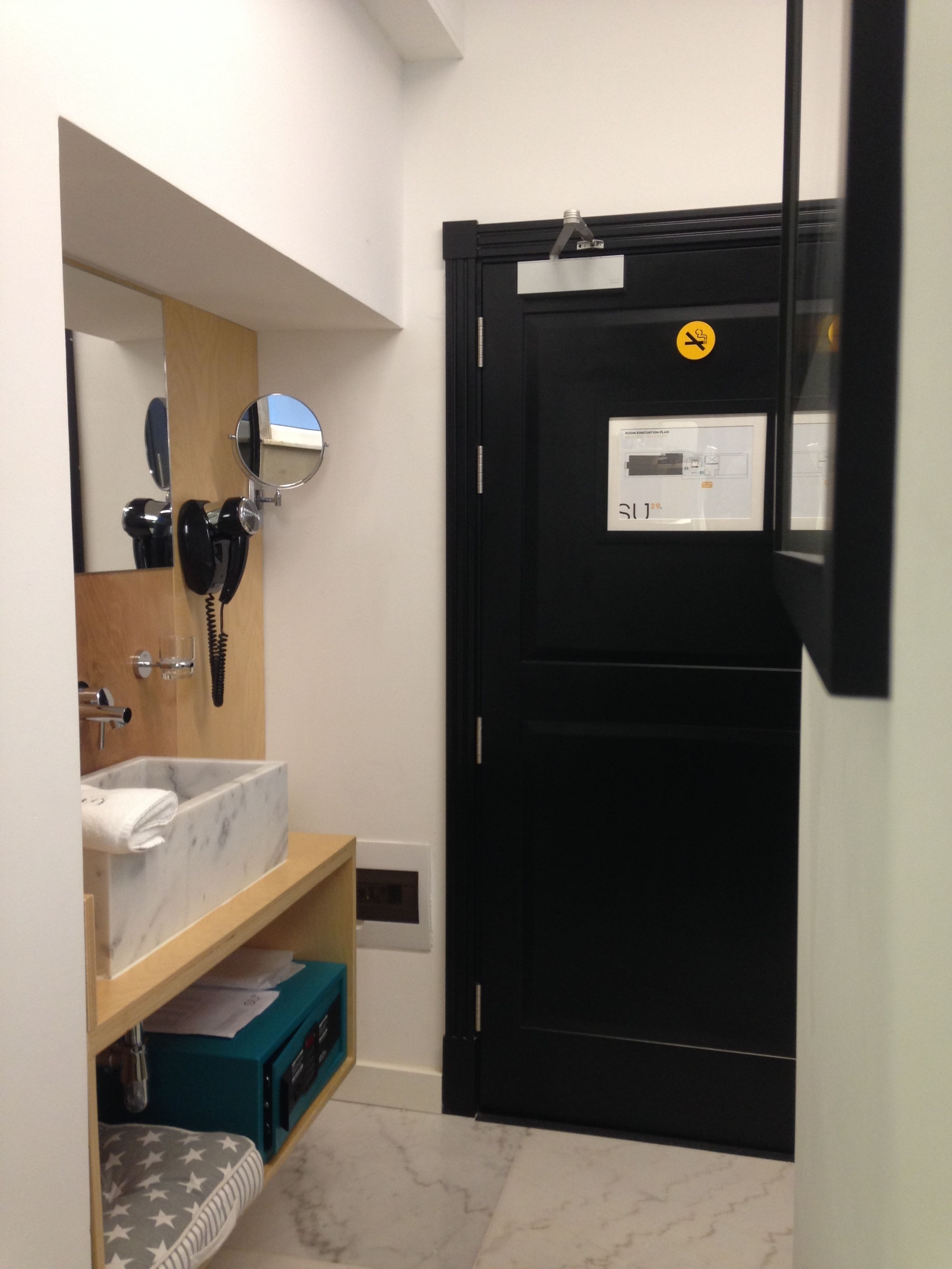 A bathroom with a marble sink, a hairdryer, a mirror, and a black door with a sign.