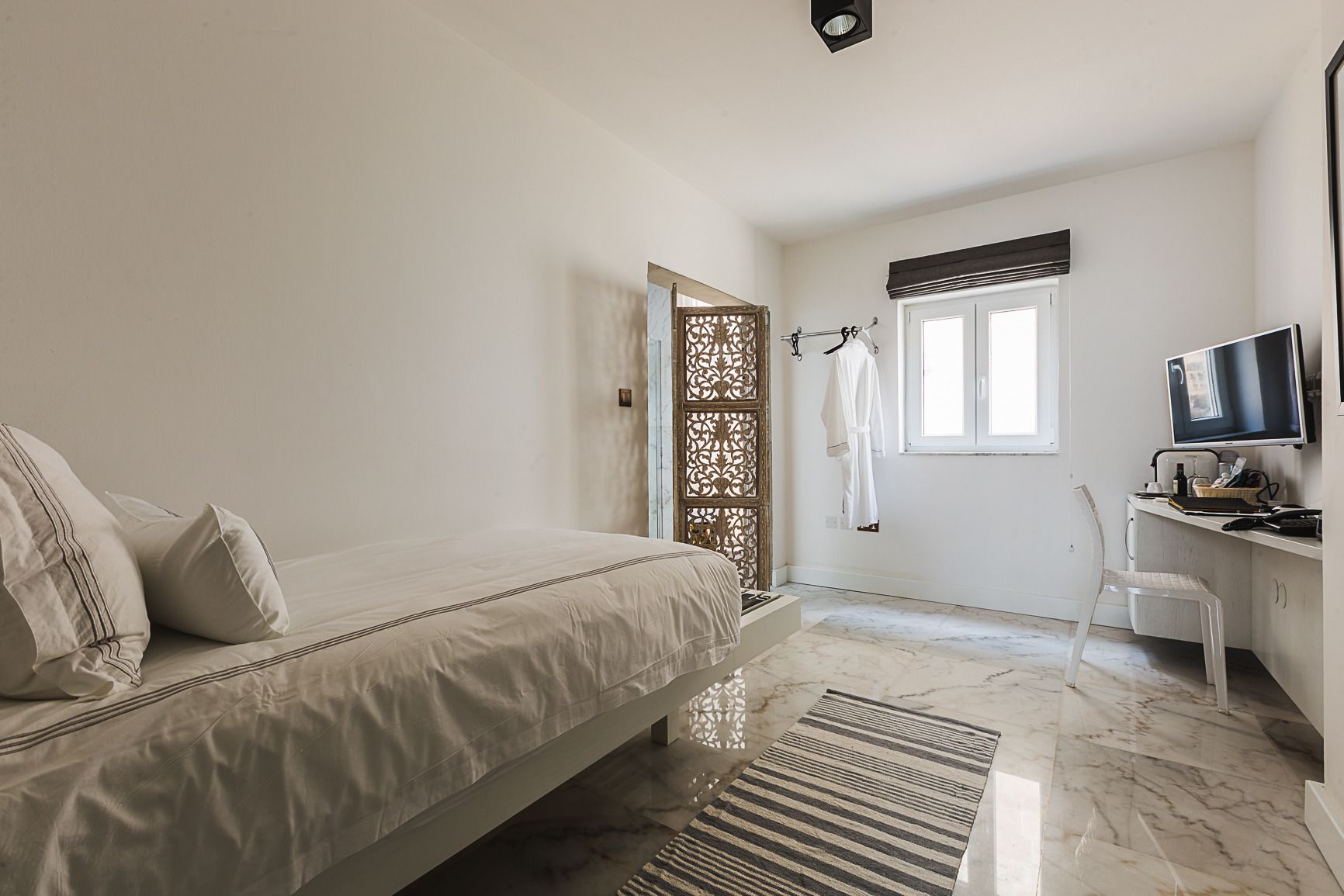 A bedroom with a bed, a desk with a computer, a chair, and a TV.