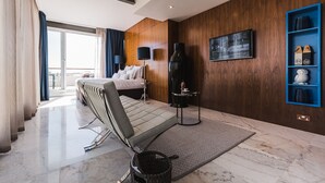 Une chambre d’hôtel moderne équipée d’un lit, d’un coin salon, d’une grande fenêtre et d’un téléviseur fixé au mur.