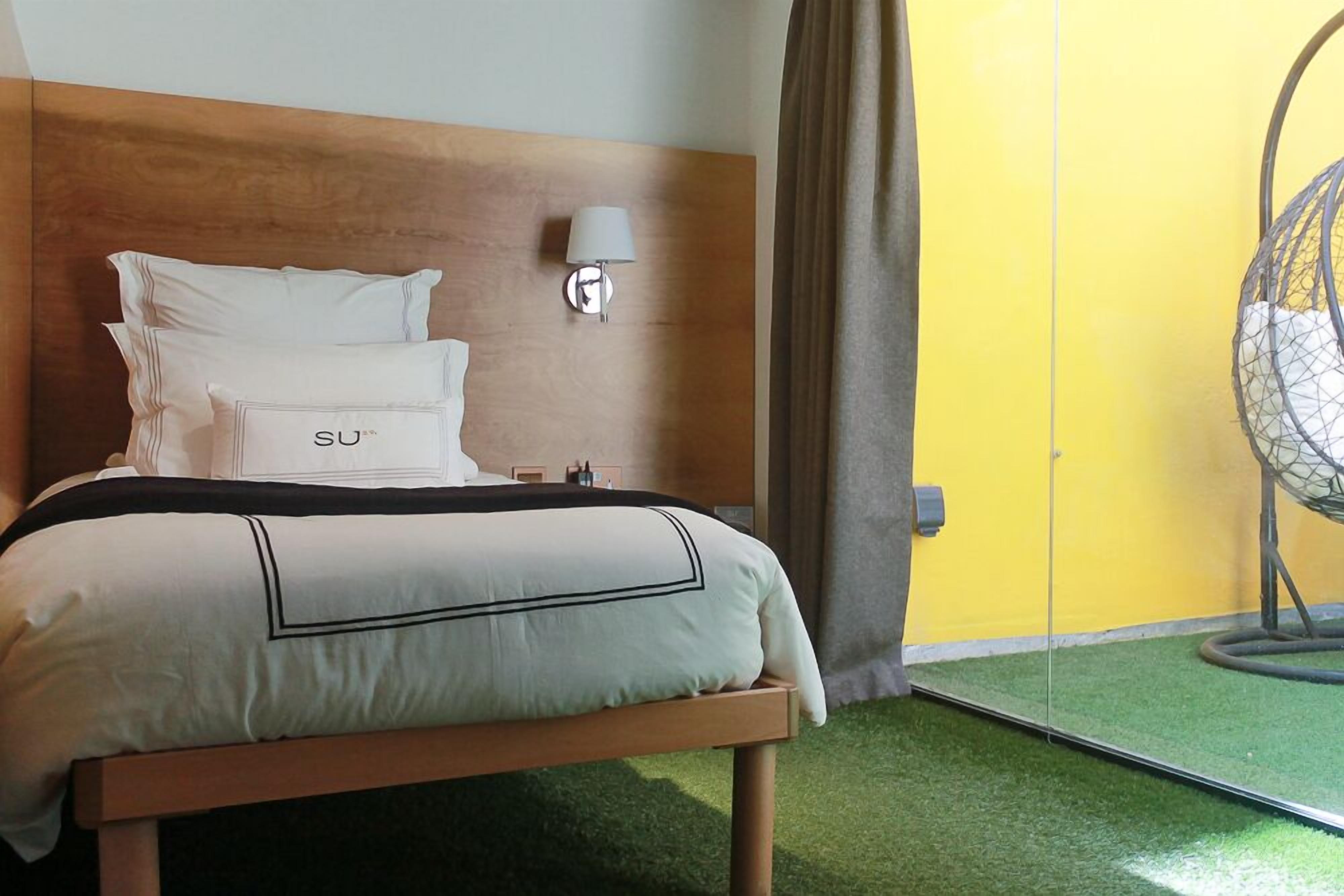 A hotel room with a bed, a wall-mounted lamp, and a hanging chair.