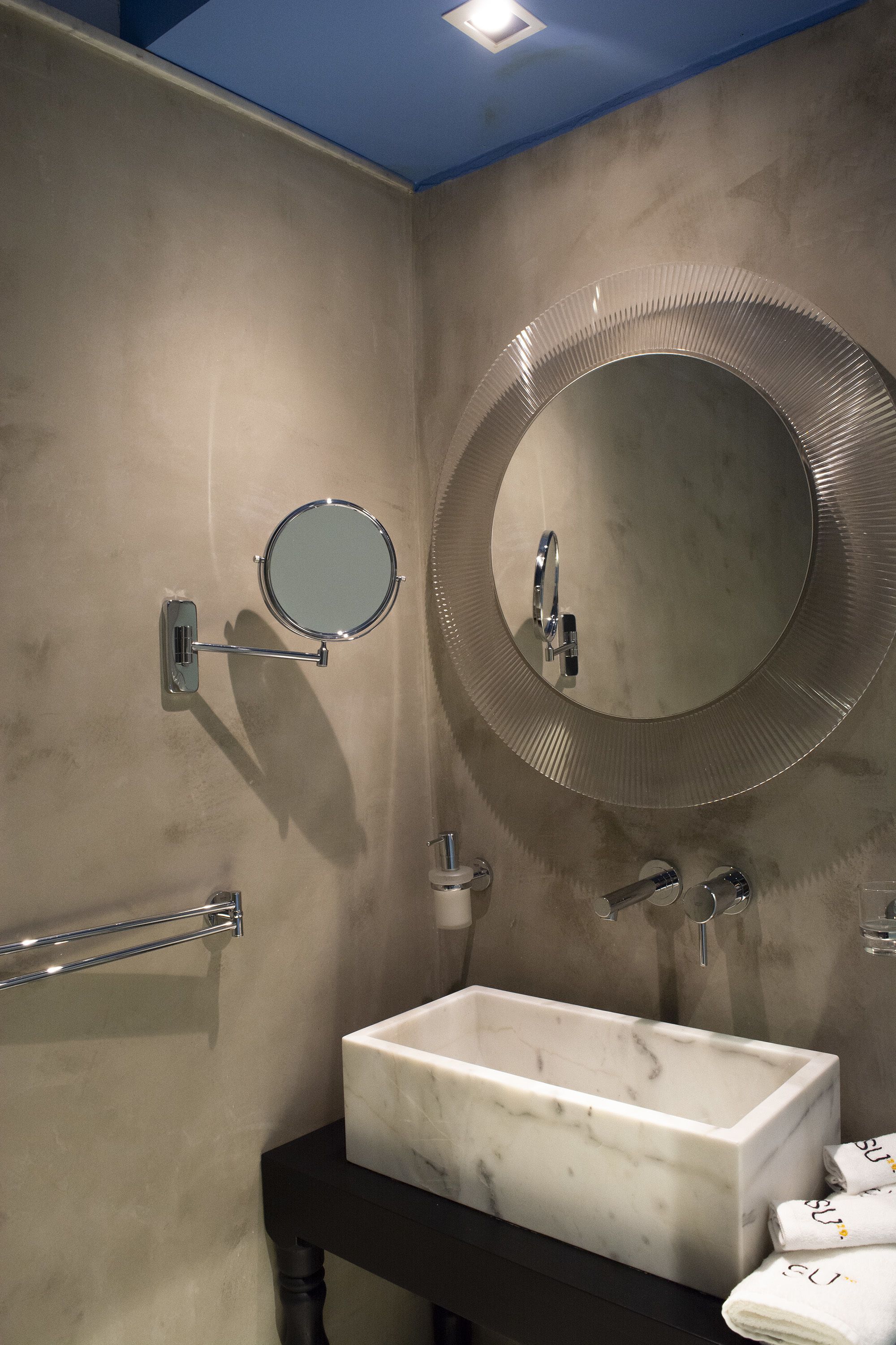 Une salle de bain avec un lavabo blanc, un miroir rond et un porte-serviettes.