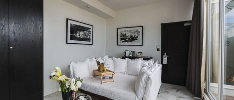 Una sala de estar moderna con un sofá blanco, una mesita con una botella de champán y un jarrón de flores. Hay dos fotografías en blanco y negro en la pared.