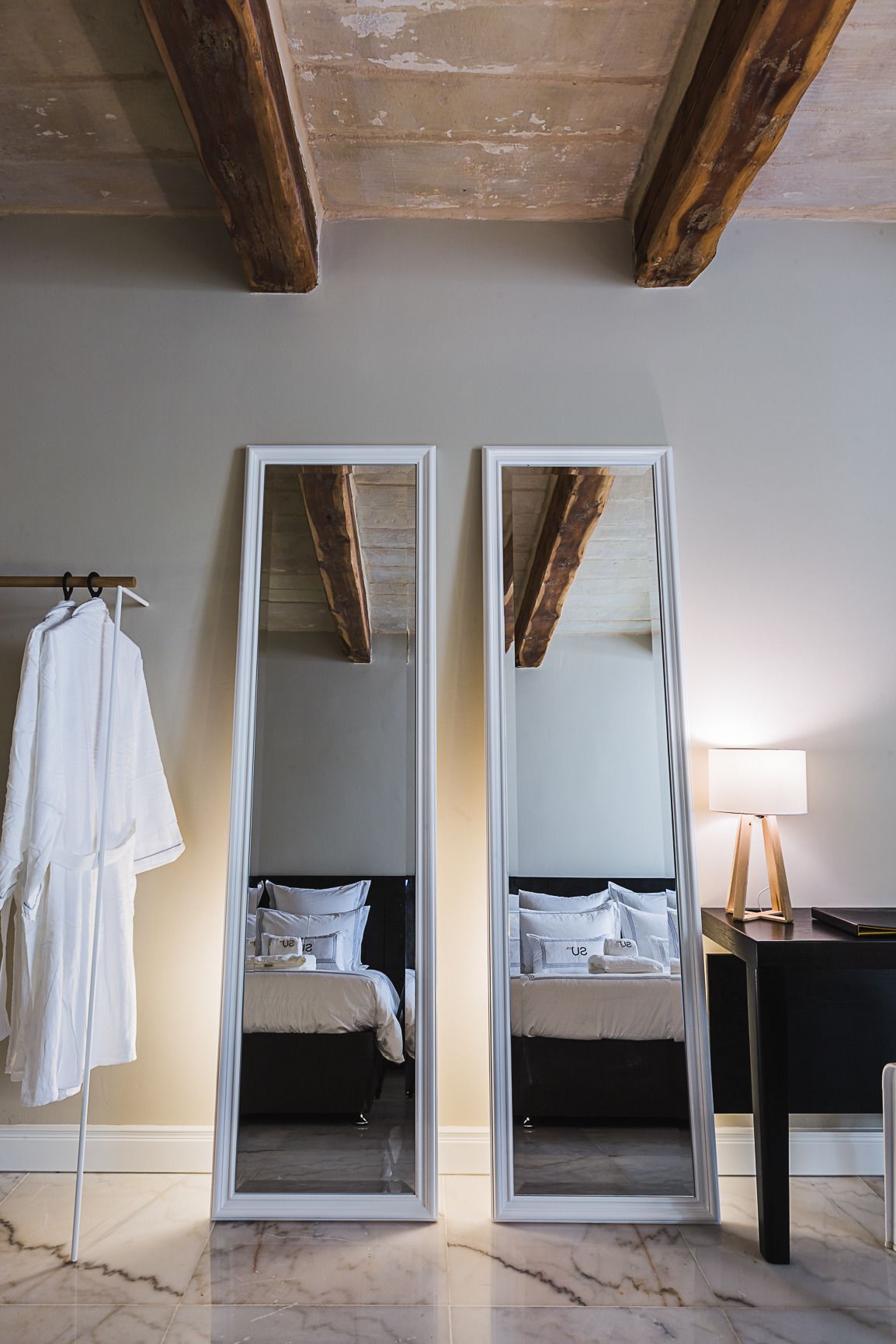 Een slaapkamer met een grote spiegel, een bed, een nachtkastje en een badjas die aan een rek hangt.