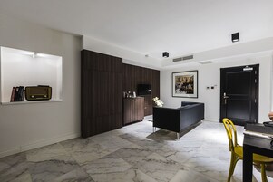 Una sala moderna con un mueble de madera oscura, un sofá negro, una mesa de comedor con sillas amarillas y un cuadro en la pared.