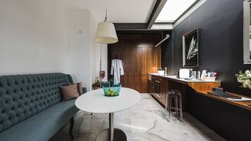 Una sala moderna con un sofá azul, una mesa redonda con una cesta azul, y una cocina con armarios de madera y encimera.