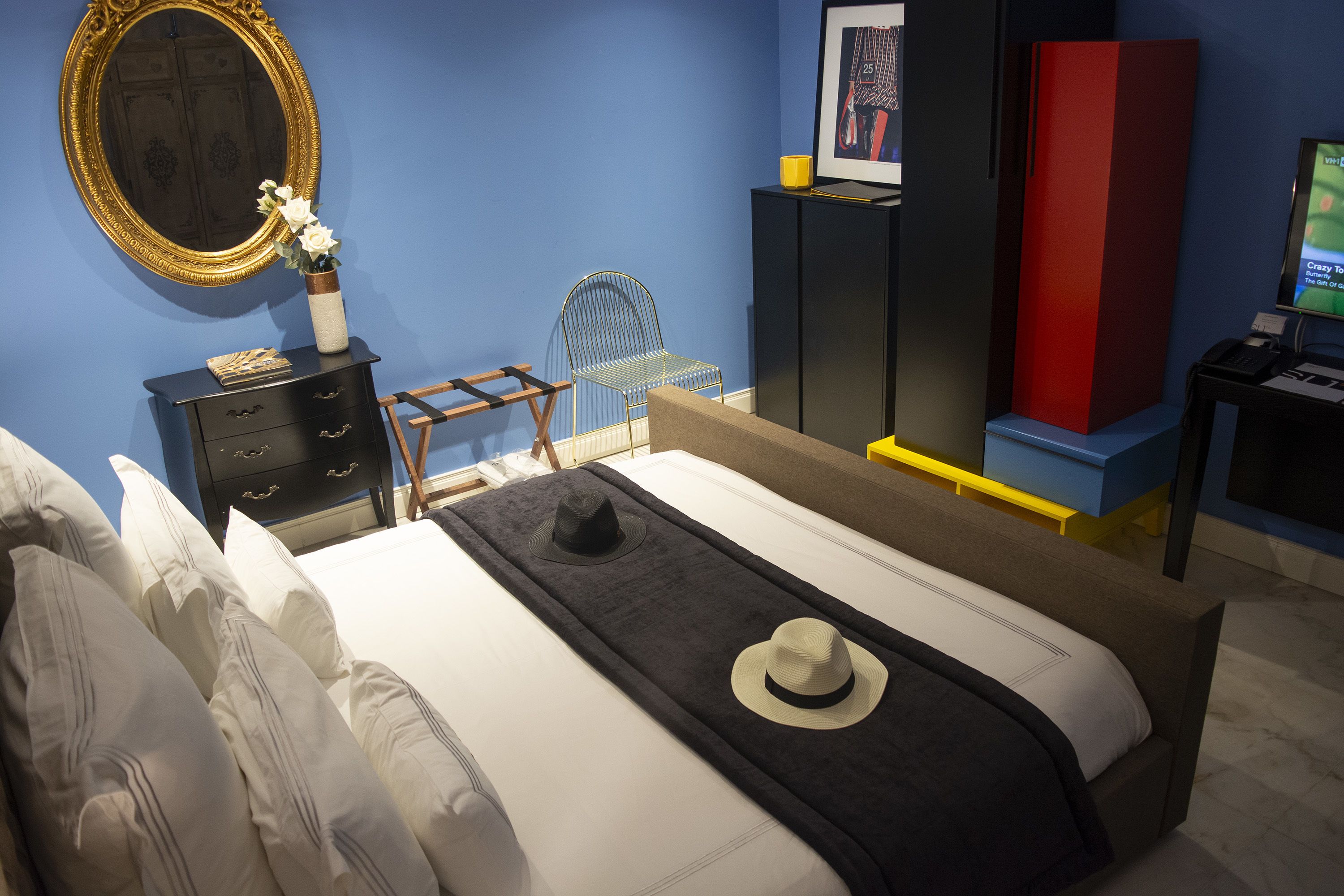 Un dormitorio con una cama, un tocador, una silla, un espejo y un televisor.
