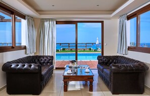 A room with a pool view, two leather sofas, a wooden coffee table, and a large sliding glass door. - Vasia Villas (Agios Nikolaos)