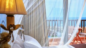 Un dormitorio con cama, lámpara y vista al océano a través de cortinas traslúcidas.