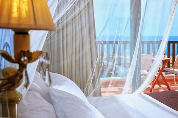 A bedroom with a bed, a lamp, and a view of the ocean through sheer curtains. - Vasia Villas (Agios Nikolaos)