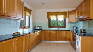 Una cocina con armarios de madera, encimera negra, ventana con vistas a zonas verdes y una lavadora.