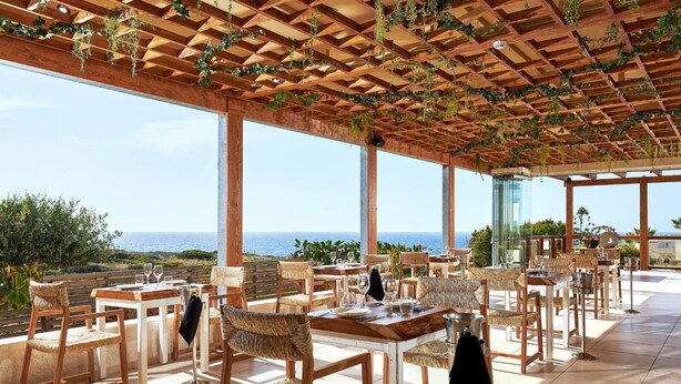 An outdoor dining area with wooden tables and wicker chairs, overlooking the sea. - Vasia Sea Retreat - Adults Only. (Agios Nikolaos)