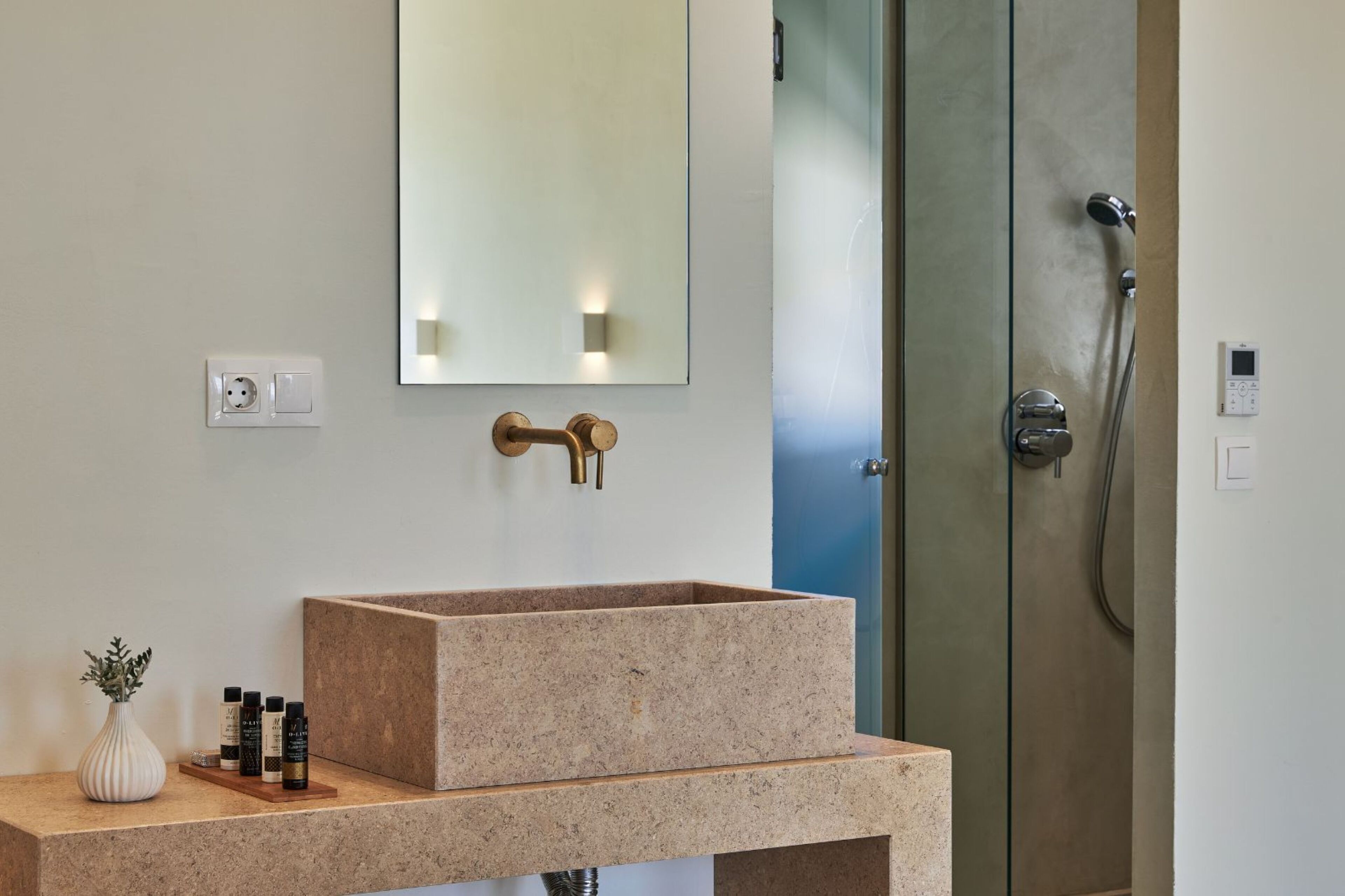 Un baño con un lavabo rectangular, un espejo, una ducha y una lámpara en la pared.