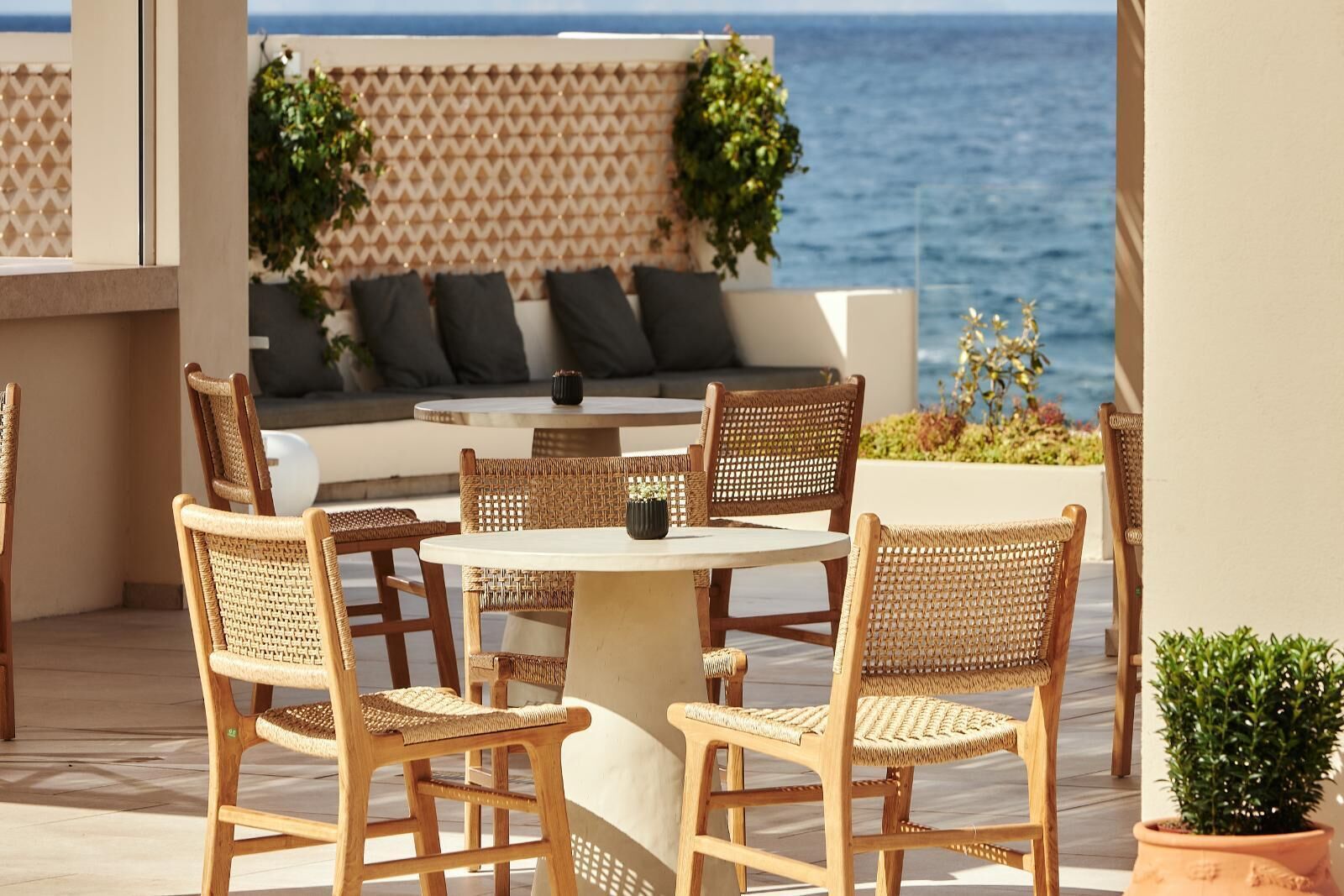 A round table with wicker chairs, a sofa with cushions, and a view of the sea.
