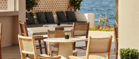 A round table with wicker chairs, a sofa with cushions, and a view of the sea.