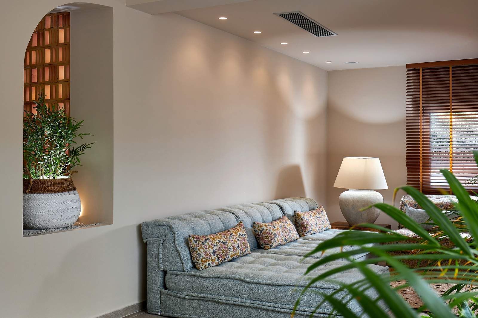 Een moderne woonkamer met een grijze bank, gestreepte kussens, een vloerlamp en een kamerplant.