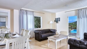 A living room with a dining area, a black leather sofa, a white table, and a view of a pool. - Elounda Eleon Villas (Agios Nikolaos)