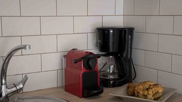 Een keuken met een spoelbak, een rode koffiemachine, een zwarte koffiepot en een bord met twee gebakjes.