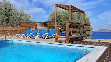 Una piscina con sillas reclinables azules y una pérgola de madera.